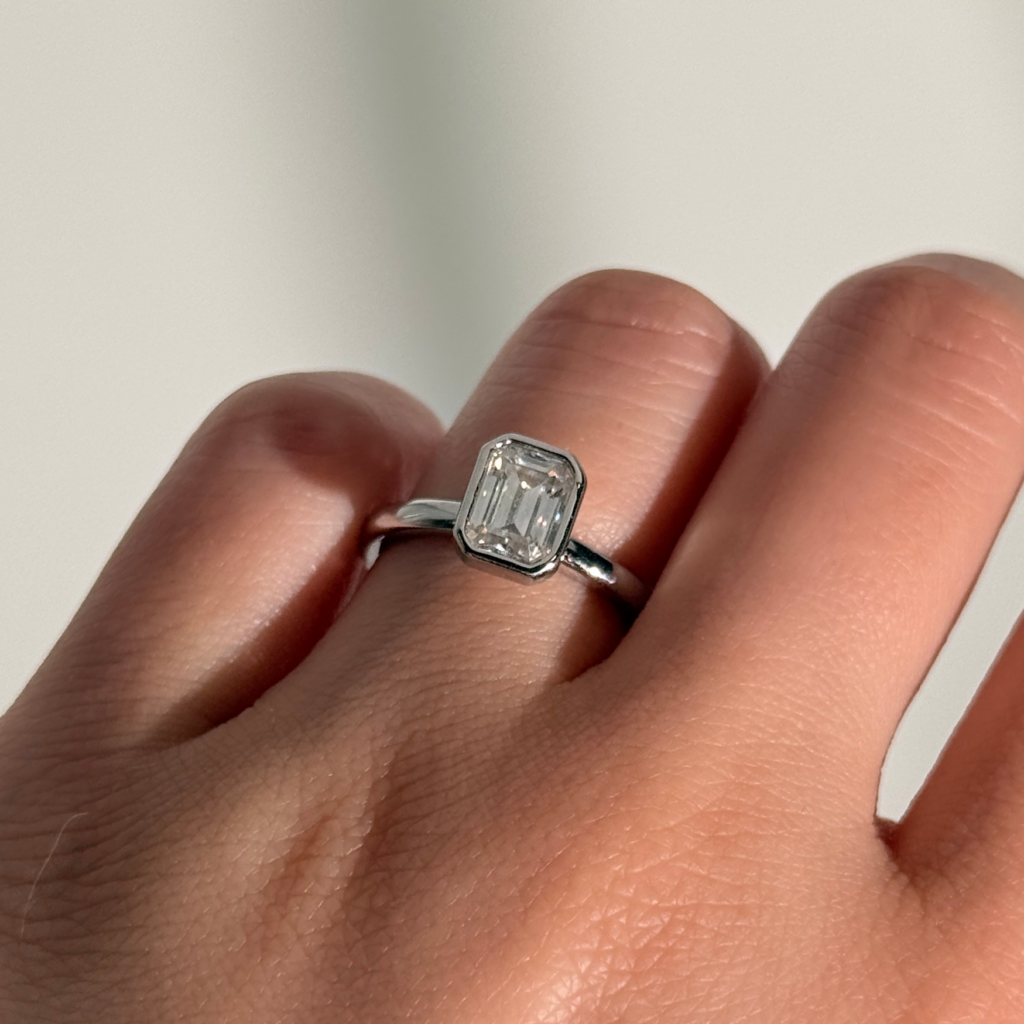 Bespoke emerald cut diamond engagement ring in white gold bezel setting